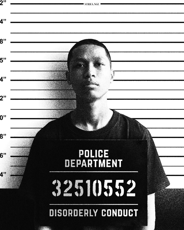 Mugshot vue de face d'un détenu tenant son matricule dans les mains et positionné devant une toile de mesure.
